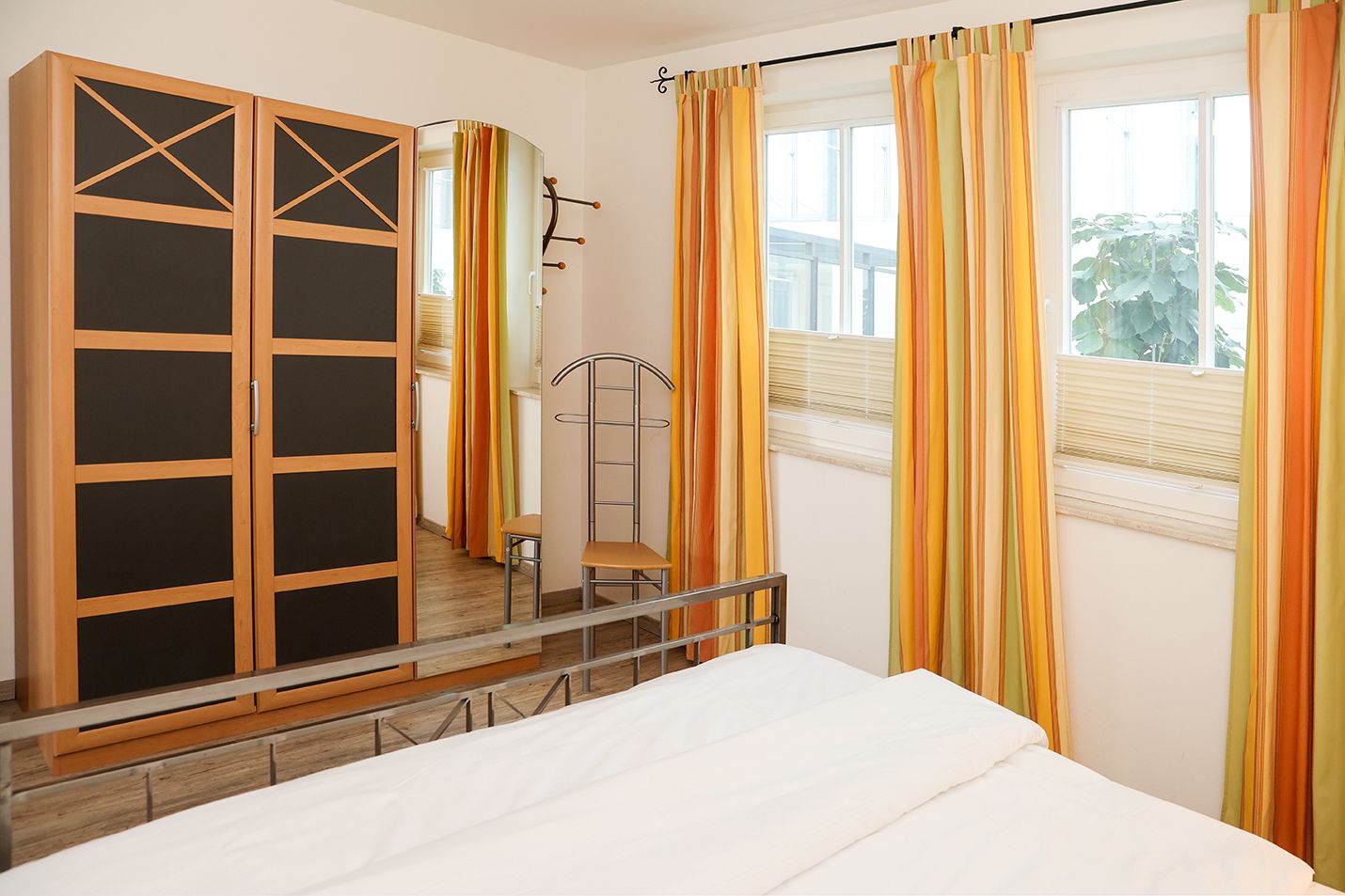 Schlafzimmer mit Metallbett, Vorhängen und Kleiderschrank